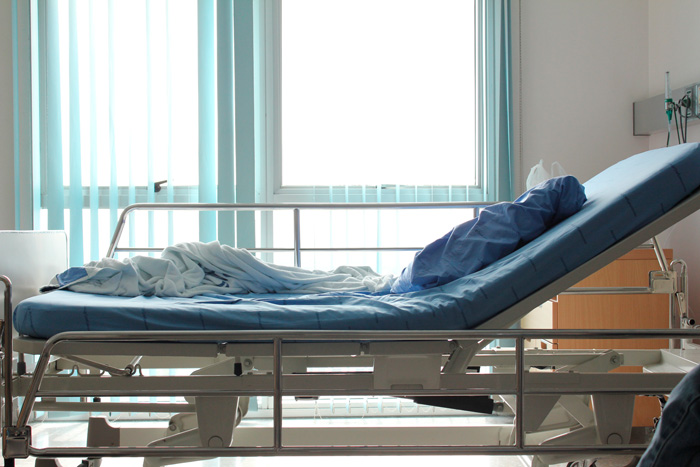 A patient's bed in front of a window in a hospital ward